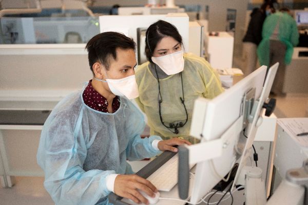 two gowned people at a computer in clinic/lab