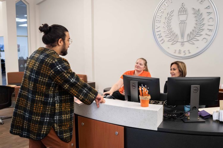 A student stands at a reception desk talking to two workers