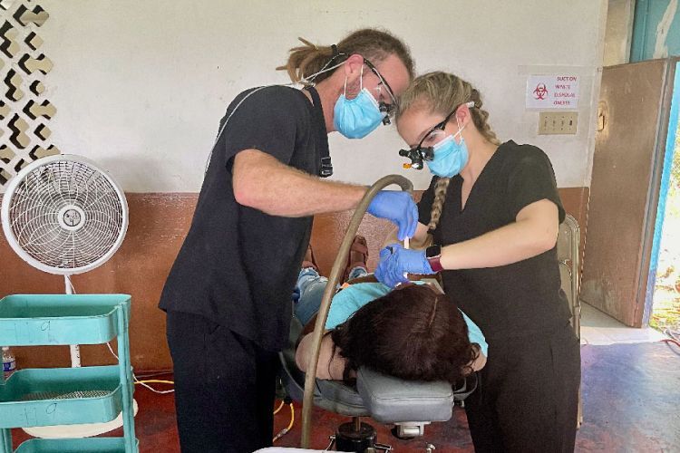 Two masked dental volunteers working with a patient who is lying down 